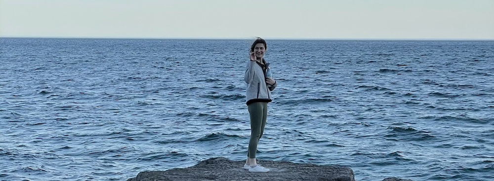 a woman standing on a large rock lakeside, waving