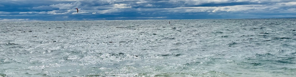 windy day, waves breaking, kite surfer in the distance, partly cloudy skies